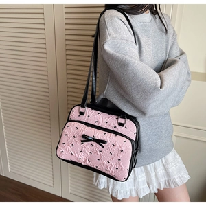 Pink fabric shoulder bag featuring black ribbon bow patterns and textured pleats on model