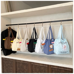 Detail of multiple canvas tote bags with cartoon towel embroidery and drawstring closure