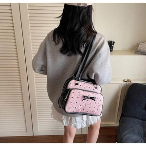 Detail of pink and black bow-knot crossbody bag with multi-zipper compartments on a model