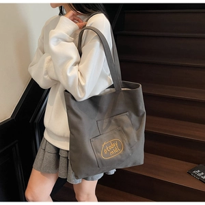 Detail of grey canvas tote bag featuring yellow #today mldl embroidery and outer pocket