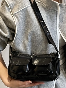 Chic black patent leather shoulder bag with dual front pockets and silver metal eyelets