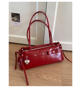 Detail of red faux leather handbag with bow decoration, silver eyelets and heart pendant
