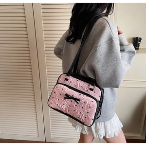 Pink pleated shoulder bag with black bow tie prints and contrast handles shown on model