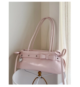 Close-up of pink leather baguette bag with metal eyelets and heart pendant detail