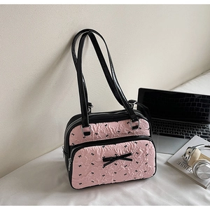 Detail of pink textured fabric with black bow patterns and dual leather straps on shoulder bag