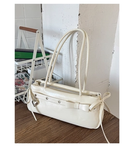 Detail of a creamy white leather handbag with bow decoration and heart charm