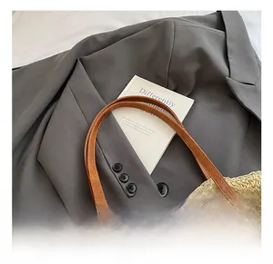Detailed close-up of brown leather handles with reinforced cross-stitching on straw tote bag