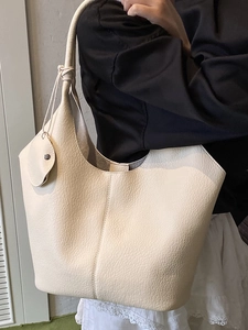 Minimalist beige lychee grain leather tote bag with knot detail and circular charm