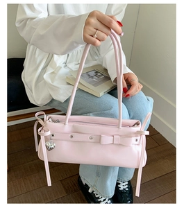 Detail of light pink leather handbag showing metallic bow eyelets and heart pendant accessory