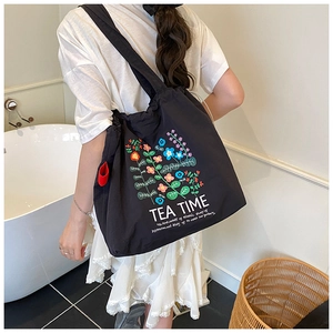 Detail of black canvas tote bag featuring floral embroidery and drawstring closure