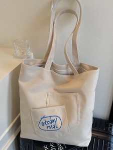 Minimalist cream canvas tote bag with long shoulder straps and blue circular embroidery