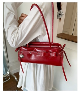 Detail view of the red glossy shoulder bag featuring a bow and heart pendant