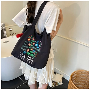 Detail of drawstring opening on black tote bag with floral pattern and tea time text