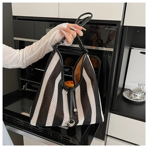 Detail of black and white striped mesh woven tote bag with leather trim and metal charm