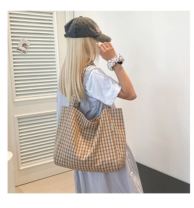 Détail du sac cabas en toile à carreaux marron avec étiquette porté à l'épaule