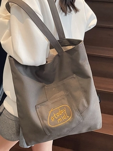 Minimalist charcoal grey canvas tote bag with yellow embroidery on a wooden background