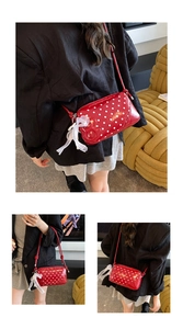 Detail of red polka dot crossbody bag featuring a large white lace bow charm accessory