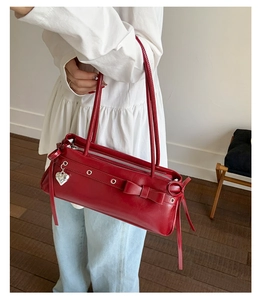 Detail of red vintage leather shoulder bag with bow and silver heart pendant charm