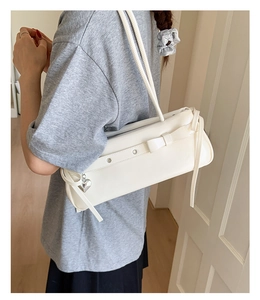 Detail of cream white underarm bag featuring a bow, metal eyelets and a heart pendant
