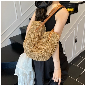Detail of hand-woven straw tote bag featuring brown leather strap and spiral texture