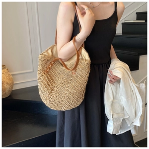 Detail of hand-woven straw tote bag with brown leather straps on a model's shoulder