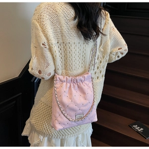 Close-up of pink quilted bucket bag with gold chain strap and metal logo on wooden stairs