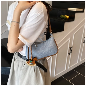 Detail of light blue denim shoulder bag with brown leather trim and horse charm pendant
