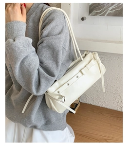 Close-up of white leather shoulder bag featuring silver eyelets and heart pendant detail