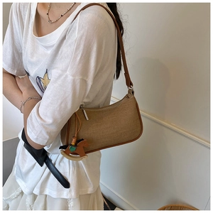 Detail view of brown canvas baguette bag with leather strap and a wooden horse pendant