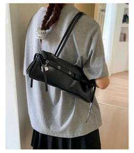 Detail of black glossy leather underarm bag with silver grommets and heart pendant detail