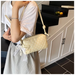 Detail of light yellow polka dot baguette bag with pearl bow charm and knot strap