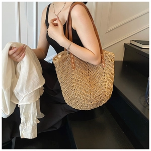 Detail of hand-woven straw tote with brown leather handles and cross-stitch craftsmanship