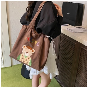 Detail of a brown tote bag with bear embroidery and adjustable drawstring closure
