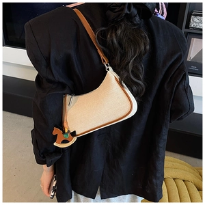 Detail of canvas shoulder bag with brown leather trim and a horse charm on a model
