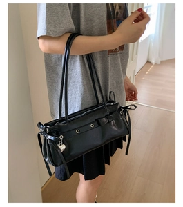 Detailed view of a black glossy shoulder bag with silver eyelets and heart pendant decor