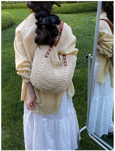 Detailed shot of summer straw tote bag with brown leather handles on natural grass