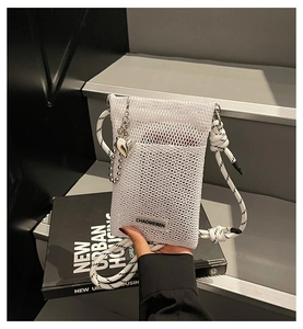 Detailed shot of white mesh phone bag with heart charm and woven strap on a book