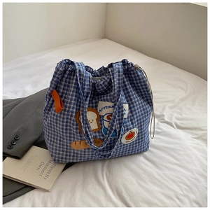 Detail of blue plaid canvas tote bag featuring embroidered bread and coffee cartoon patches