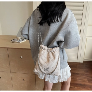 Detail of cream quilted bucket bag with chain strap and stud accents in casual setting