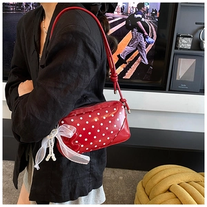 Detail of red polka dot shoulder bag featuring organza bow and pearl charm accents