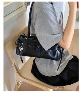 Detail of black glossy leather bag with silver eyelets and heart pendant accessory