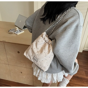 Detail of cream quilted bucket bag with silver studs, chain strap and drawstring closure