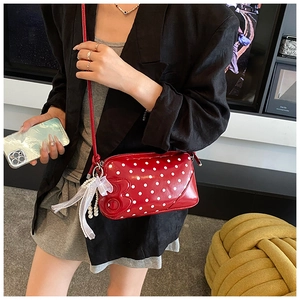 Detail of red polka dot baguette bag featuring glossy finish and lace bow with pearl charm