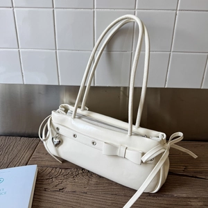 Detail of cream white leather baguette bag featuring bow decoration and silver heart charm