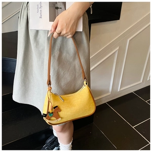 Close-up of yellow canvas underarm bag with brown leather strap and wooden horse charm