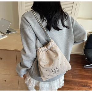 Detail of beige quilted bucket bag with silver chain strap and metal rivet accents