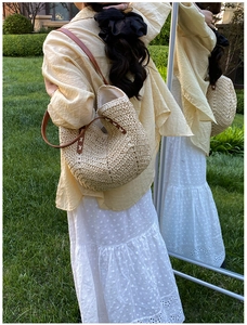 Detail of straw woven tote bag featuring dark brown leather handles and rustic weave