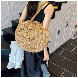 Detail of a round woven straw beach bag with hollow-out patterns and brown leather handles