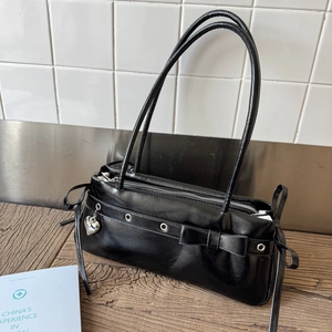 Close-up of black glossy handbag featuring silver heart pendant and bow detailing