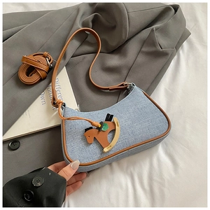Detail view of light blue denim hobo bag with brown leather trim and horse pendant